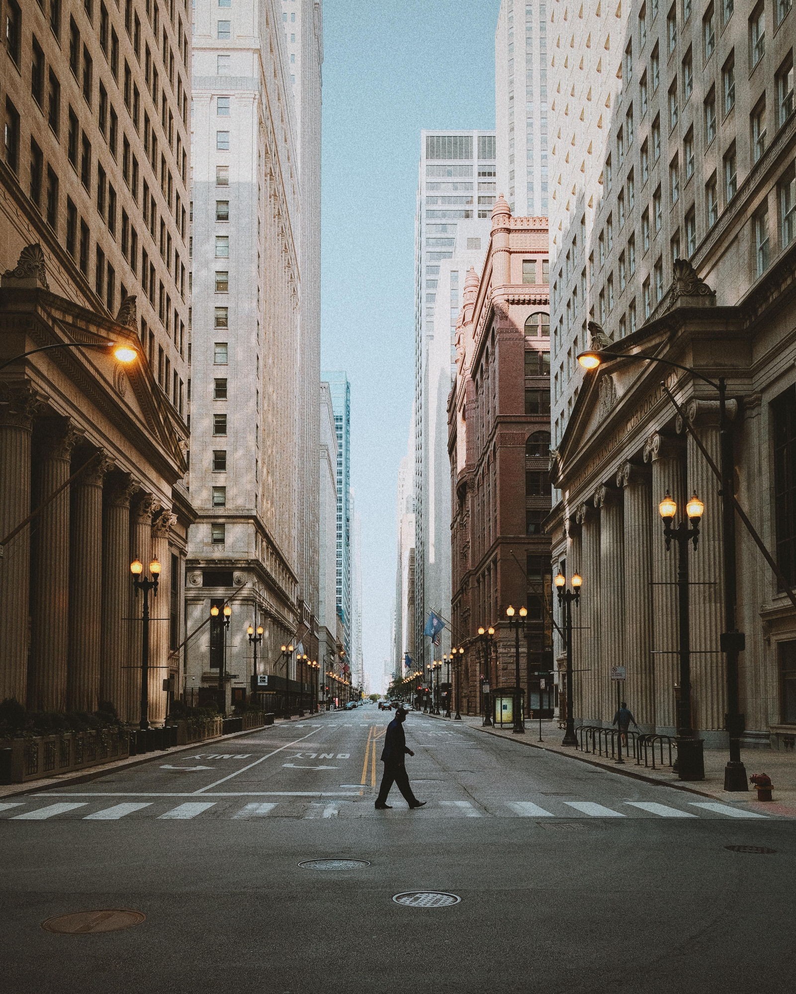 A man walks in a city between tall rows of buildings with large columns.