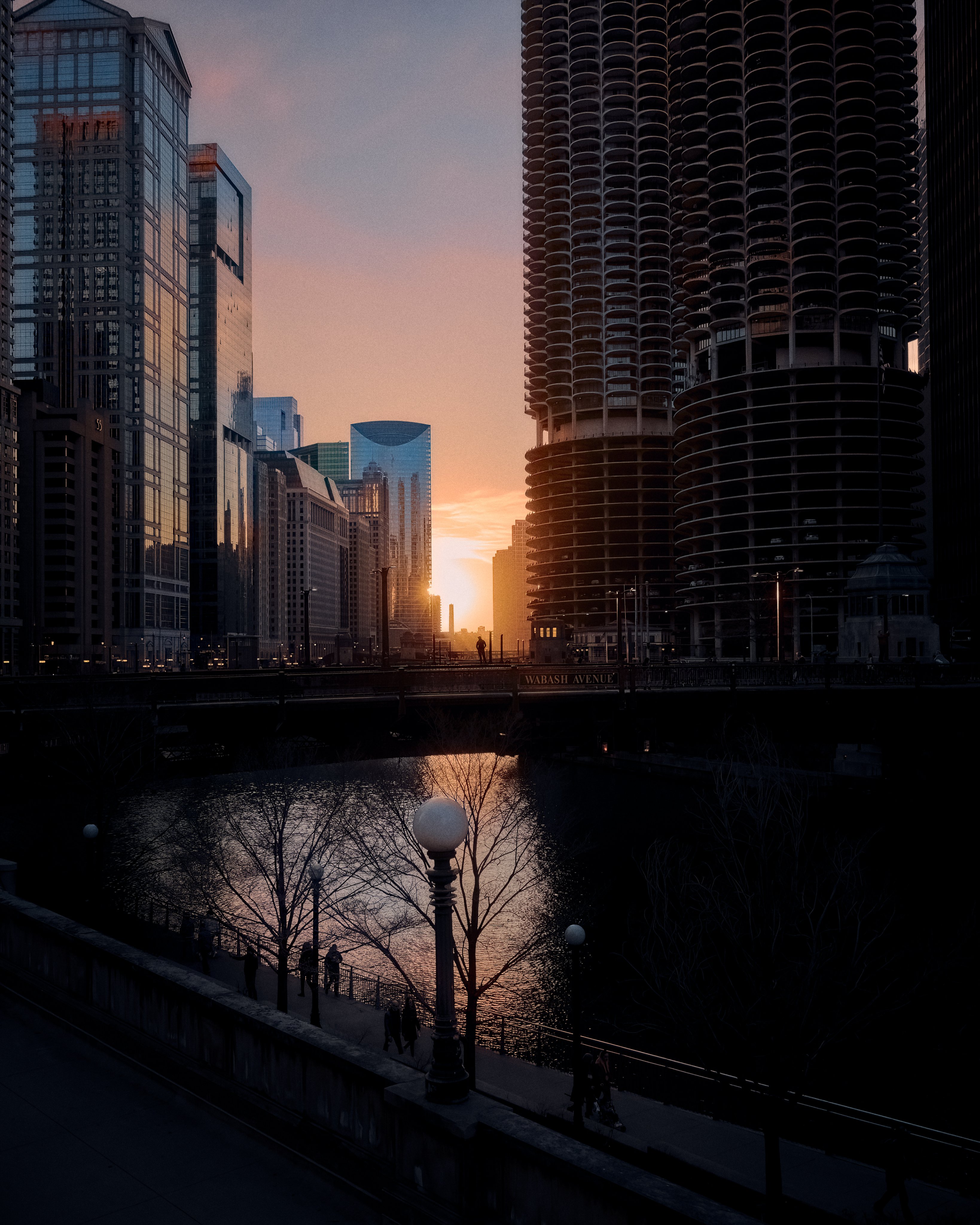 A man stands on the Wabash bridge over the Chicago River, silhouetted by the setting sun.