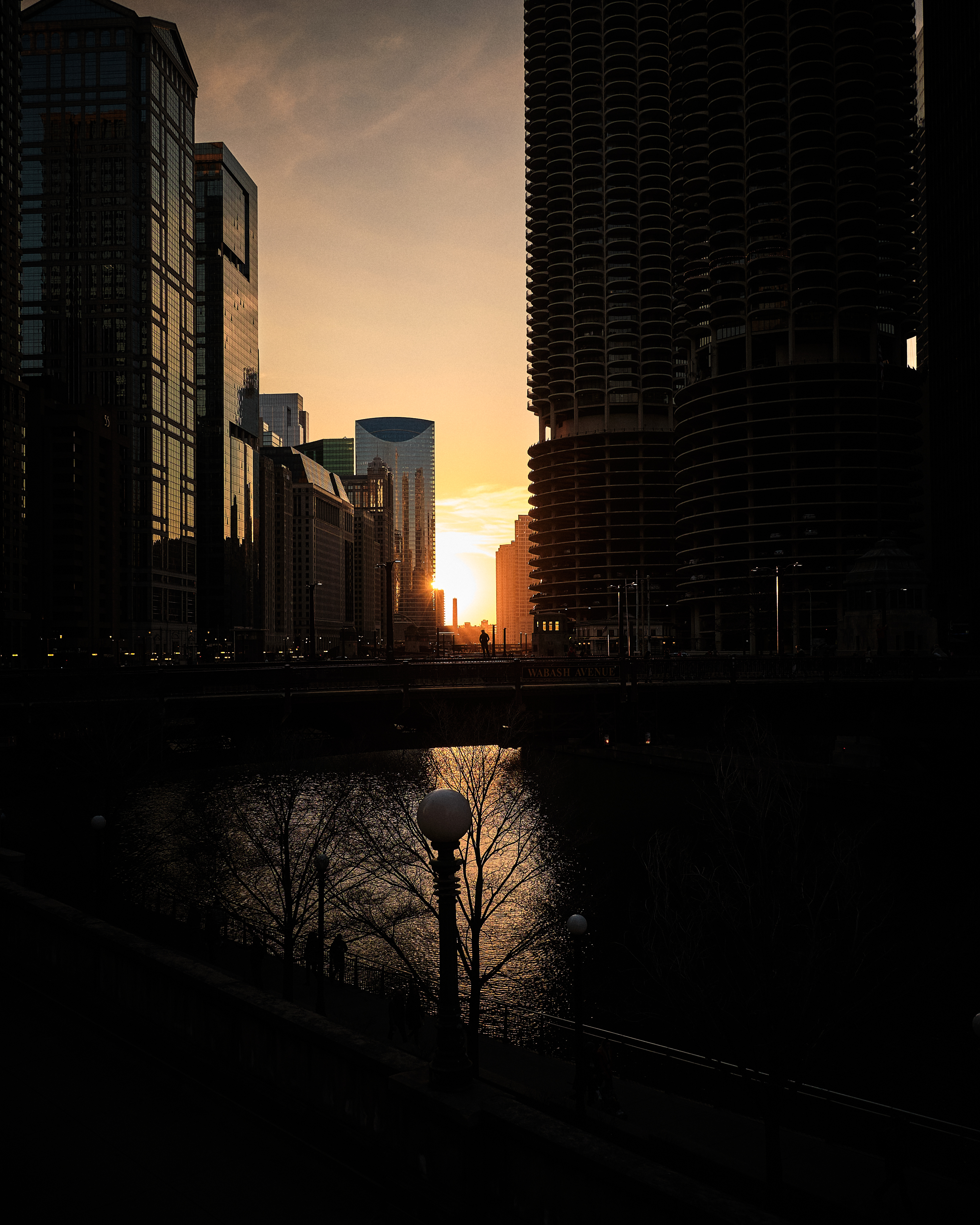 A man stands on the Wabash bridge over the Chicago River, silhouetted by the setting sun.