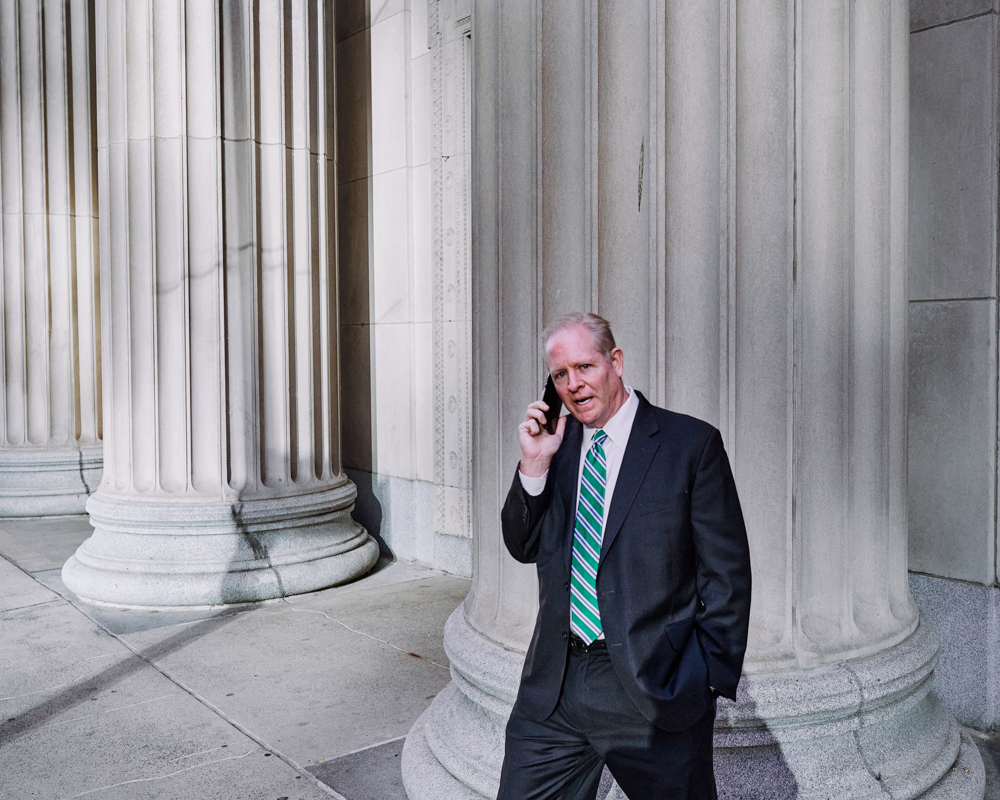 A man in a suit walks towards camera while he's talking on the phone.