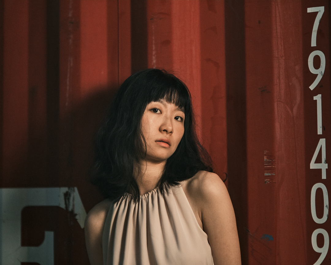 A woman poses against a red shipping container.